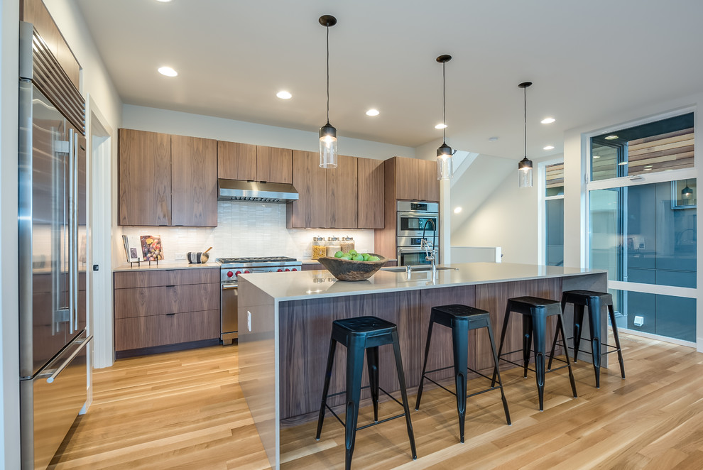 Contemporary l-shaped kitchen in Seattle with a drop-in sink, flat-panel cabinets, dark wood cabinets, white splashback, stainless steel appliances, medium hardwood floors and with island.
