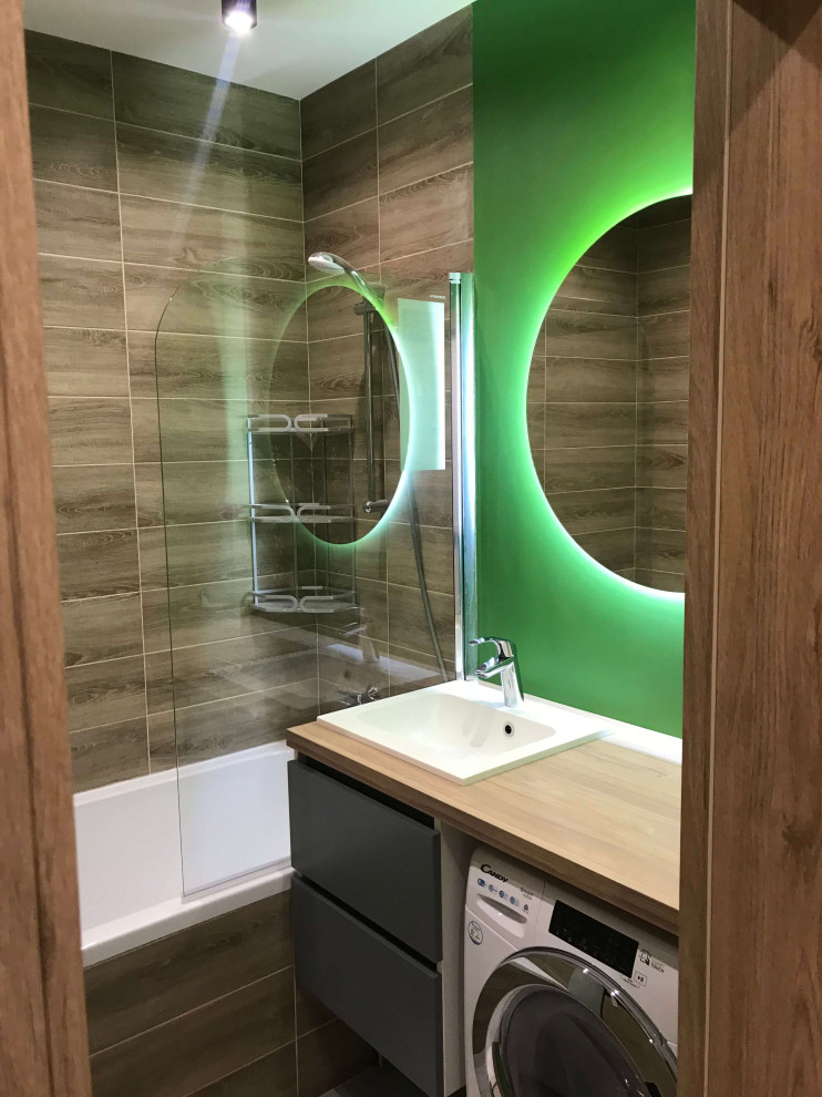 Идея дизайна: главная ванная комната среднего размера в современном стиле с плоскими фасадами, серыми фасадами, полновстраиваемой ванной, душем над ванной, инсталляцией, коричневой плиткой, керамической плиткой, зелеными стенами, полом из керамической плитки, врезной раковиной, столешницей из дерева, коричневым полом, коричневой столешницей, зеркалом с подсветкой, тумбой под одну раковину и подвесной тумбой