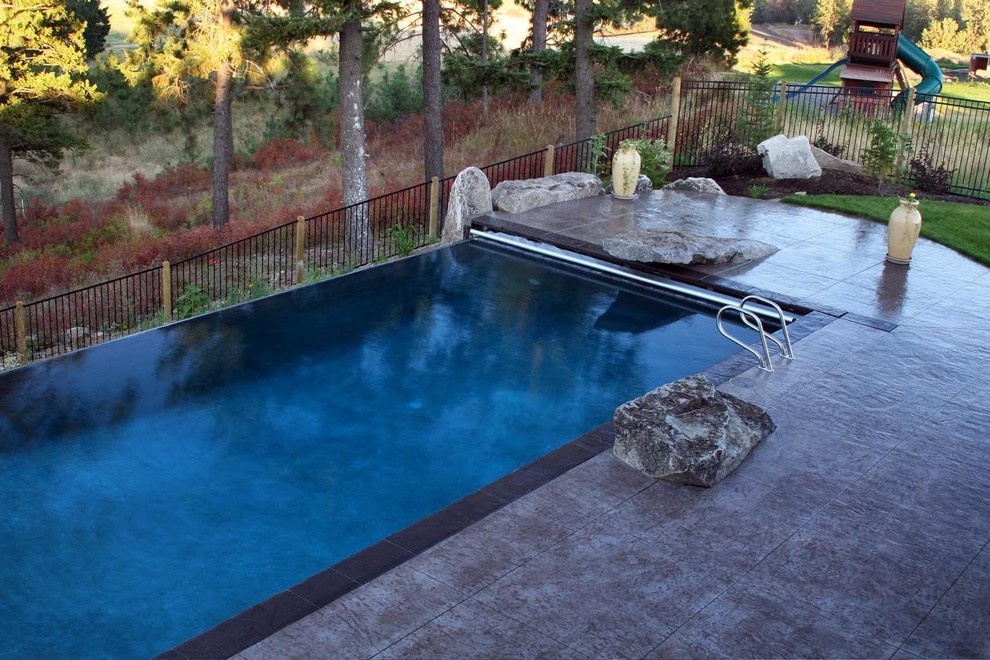 Photo of a mid-sized transitional backyard rectangular infinity pool in Seattle with stamped concrete.