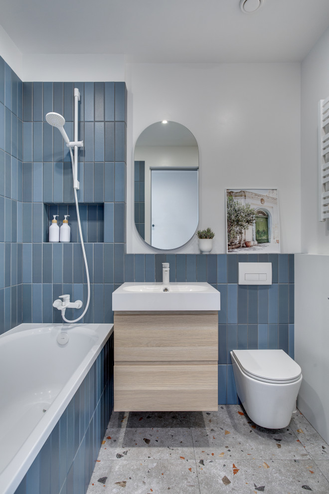 Photo of a mid-sized contemporary master bathroom in Moscow with light wood cabinets, an undermount tub, a wall-mount toilet, blue tile, ceramic tile, white walls, porcelain floors, a drop-in sink, multi-coloured floor, a single vanity and a floating vanity.