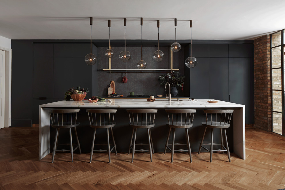 Photo of a large contemporary single-wall eat-in kitchen in London with black cabinets, marble benchtops, with island, an undermount sink, flat-panel cabinets, beige splashback, panelled appliances, medium hardwood floors, brown floor and white benchtop.