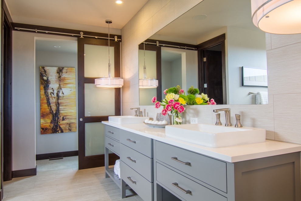 Photo of an expansive modern master bathroom in Other with flat-panel cabinets, grey cabinets, a freestanding tub, an open shower, a one-piece toilet, beige tile, porcelain tile, beige walls, porcelain floors, a vessel sink, engineered quartz benchtops, beige floor and a hinged shower door.