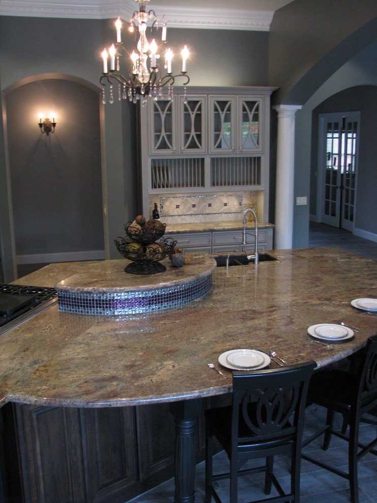 Huge transitional l-shaped porcelain tile open concept kitchen photo in Phoenix with an undermount sink, raised-panel cabinets, gray cabinets, granite countertops, gray backsplash, stone tile backsplash, stainless steel appliances and an island