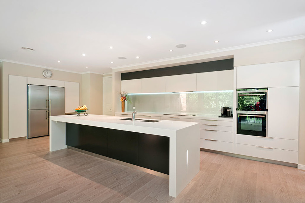 Photo of a modern galley kitchen pantry in Melbourne with an undermount sink, flat-panel cabinets, white cabinets, solid surface benchtops, metallic splashback, glass sheet splashback, stainless steel appliances and with island.