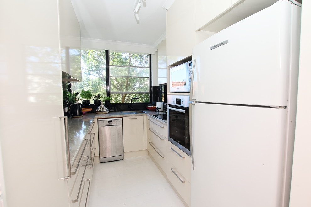 Photo of a small contemporary u-shaped separate kitchen in Sydney with a single-bowl sink, flat-panel cabinets, beige cabinets, laminate benchtops, black splashback, glass sheet splashback, stainless steel appliances, laminate floors, no island and white floor.