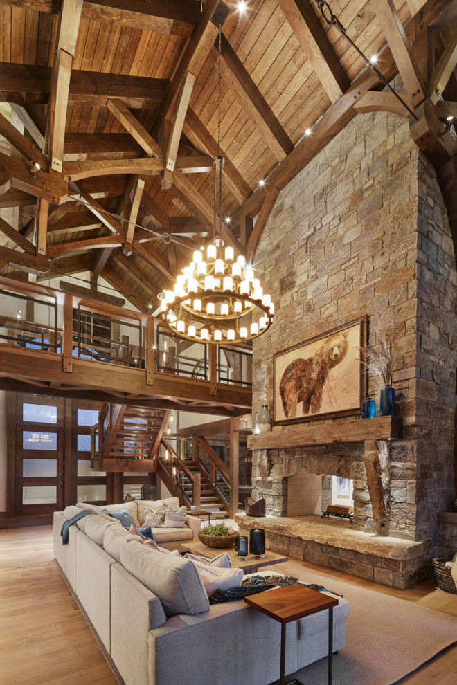 Design ideas for an expansive country open concept living room in Other with a two-sided fireplace, a stone fireplace surround, a concealed tv, exposed beam, vaulted, wood, yellow walls, medium hardwood floors and brown floor.