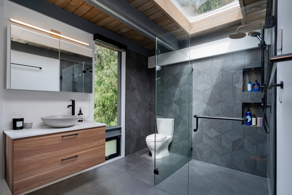 Photo of a contemporary bathroom in Los Angeles with flat-panel cabinets, medium wood cabinets, a corner shower, white walls, a vessel sink, grey floor, a hinged shower door and white benchtops.