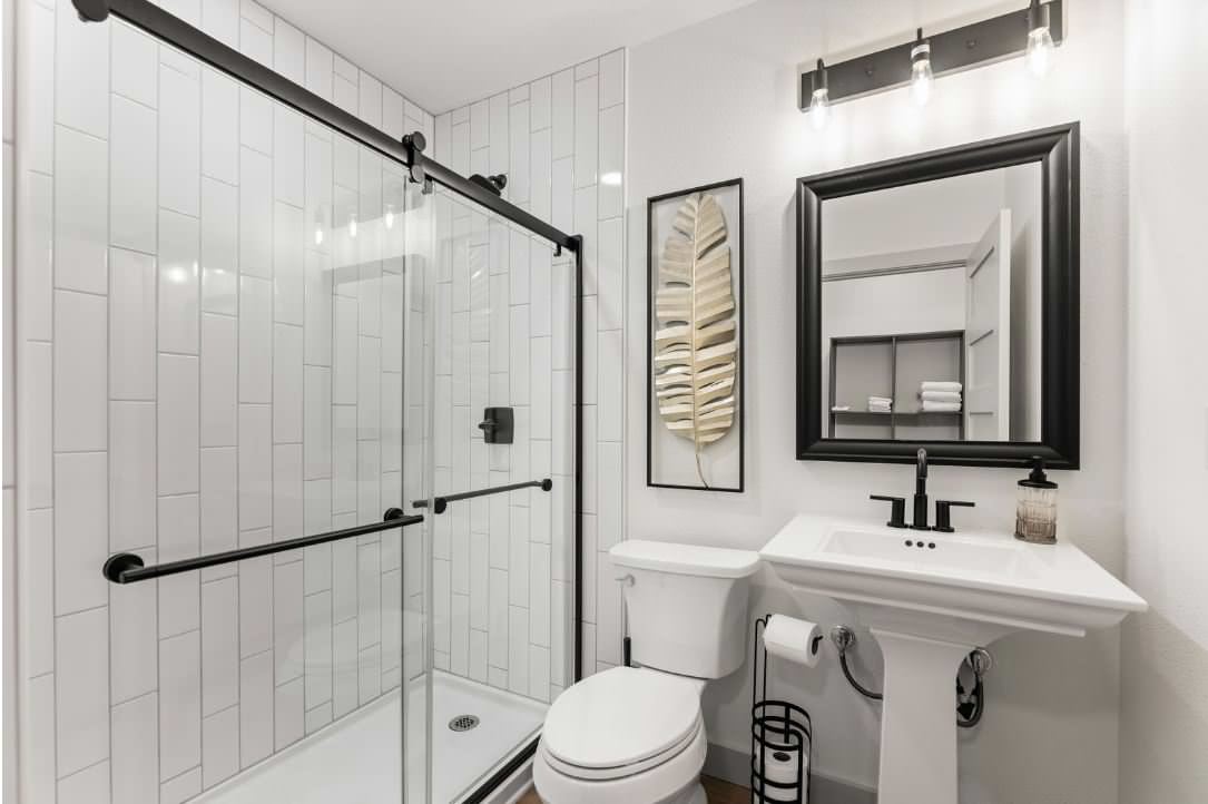 Full size shower with matching vertical 1/3 offset tile. toilet and pedestal sink.