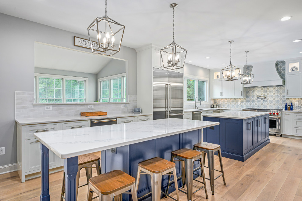 Inspiration for a large transitional l-shaped light wood floor kitchen remodel in DC Metro with an undermount sink, shaker cabinets, white cabinets, quartz countertops, white backsplash, stainless steel appliances, two islands and white countertops