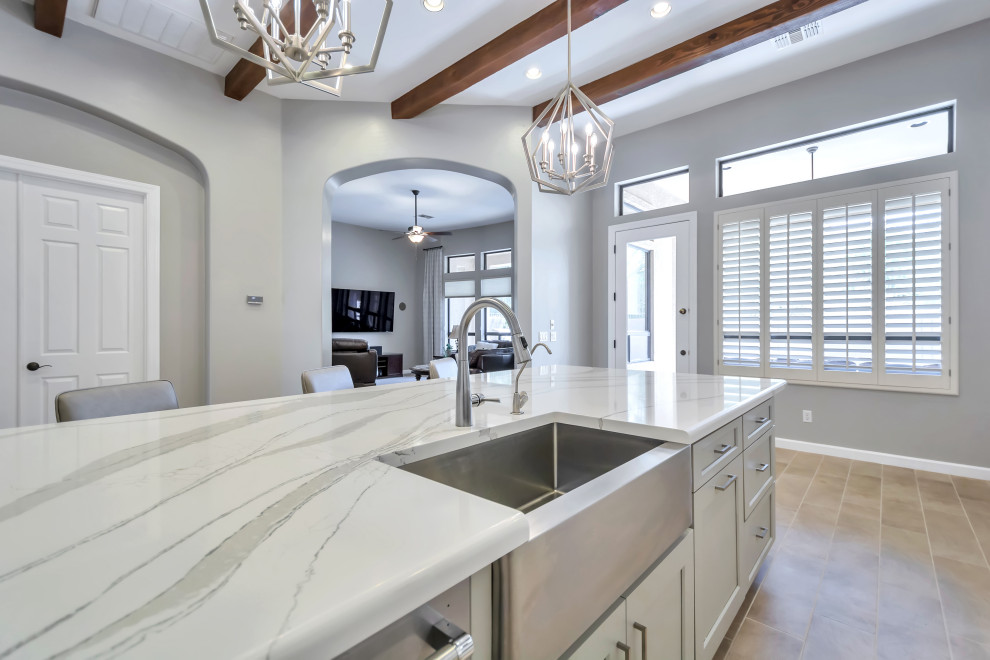 Inspiration for a large transitional l-shaped porcelain tile and brown floor eat-in kitchen remodel in Phoenix with a farmhouse sink, shaker cabinets, white cabinets, quartz countertops, white backsplash, subway tile backsplash, stainless steel appliances, an island and gray countertops