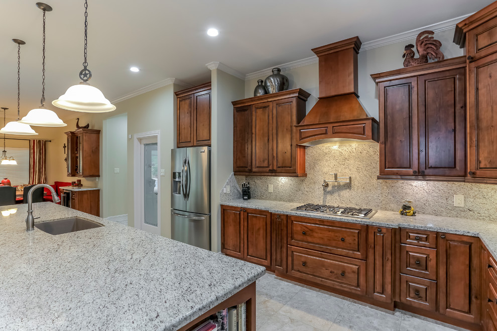 Photo of a country l-shaped open plan kitchen in Houston with raised-panel cabinets, medium wood cabinets, stainless steel appliances, with island, an undermount sink, granite benchtops, grey splashback, stone slab splashback and travertine floors.