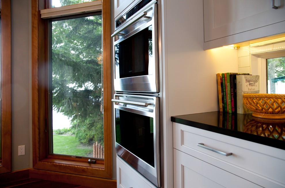 Inspiration for a large transitional l-shaped medium tone wood floor and brown floor eat-in kitchen remodel with a farmhouse sink, shaker cabinets, white cabinets, quartzite countertops, blue backsplash, glass sheet backsplash, stainless steel appliances and an island