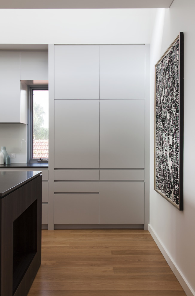 Design ideas for a large contemporary galley eat-in kitchen in Sydney with an undermount sink, grey cabinets, granite benchtops, grey splashback, glass sheet splashback, stainless steel appliances, light hardwood floors, with island and beige floor.