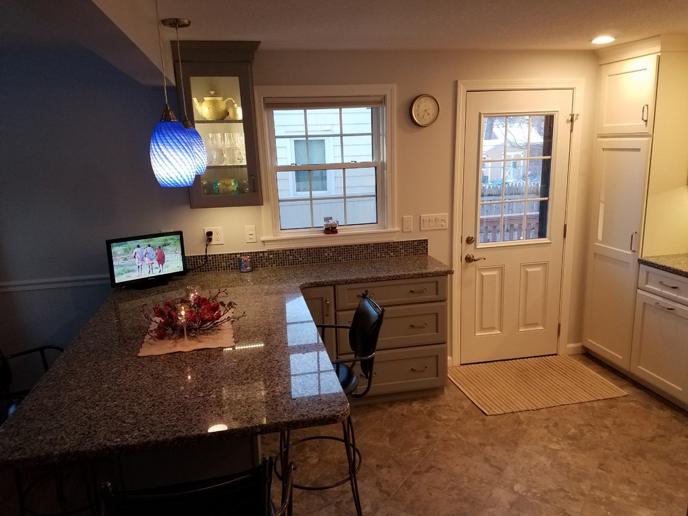 Inspiration for a mid-sized transitional brown floor and ceramic tile eat-in kitchen remodel in Boston with a double-bowl sink, shaker cabinets, white cabinets, granite countertops, white backsplash, ceramic backsplash, stainless steel appliances and a peninsula