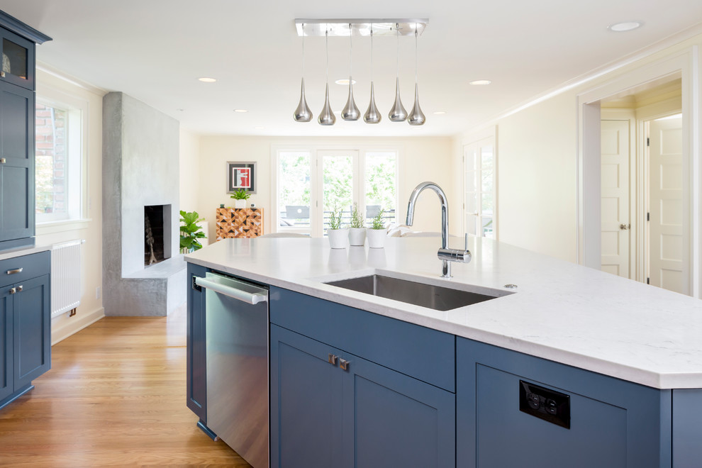 Inspiration for a mid-sized transitional l-shaped medium tone wood floor and brown floor open concept kitchen remodel in Seattle with an undermount sink, shaker cabinets, blue cabinets, solid surface countertops, white backsplash, stone slab backsplash, stainless steel appliances, an island and white countertops