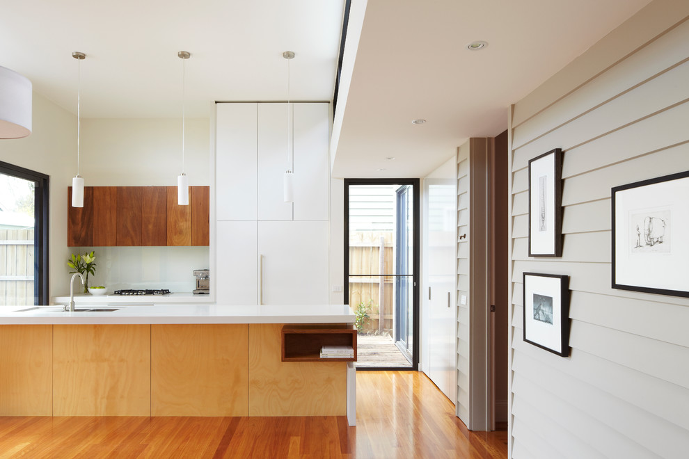 Inspiration for a mid-sized modern galley eat-in kitchen in Melbourne with an undermount sink, flat-panel cabinets, light wood cabinets, quartz benchtops, white splashback, glass sheet splashback, stainless steel appliances, light hardwood floors and with island.