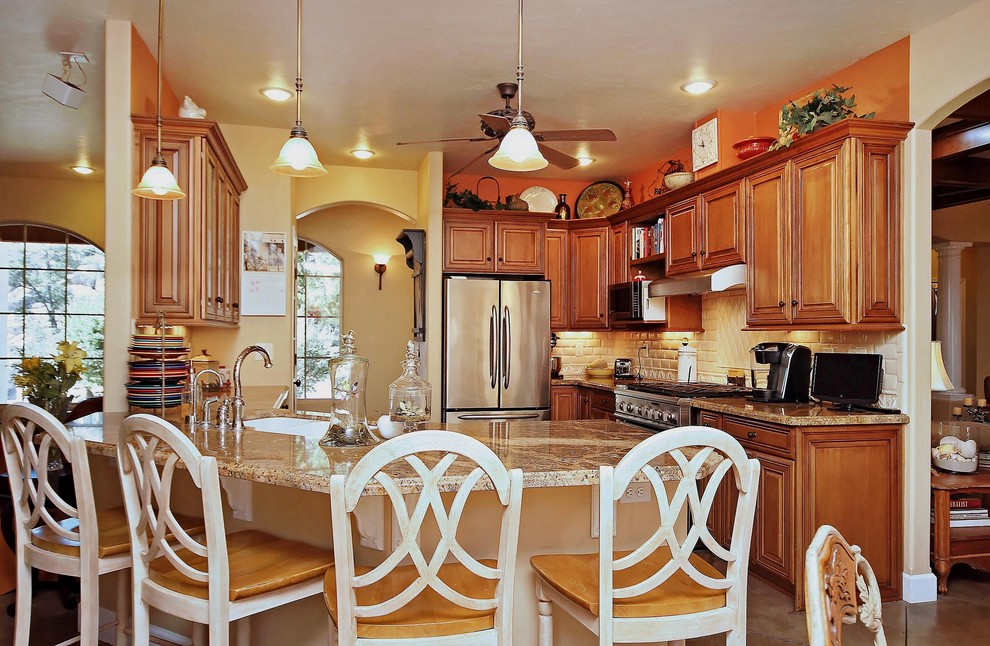 Inspiration for a mid-sized traditional l-shaped eat-in kitchen in Phoenix with raised-panel cabinets, medium wood cabinets, granite benchtops, beige splashback, subway tile splashback, stainless steel appliances, an undermount sink, concrete floors, a peninsula and brown floor.