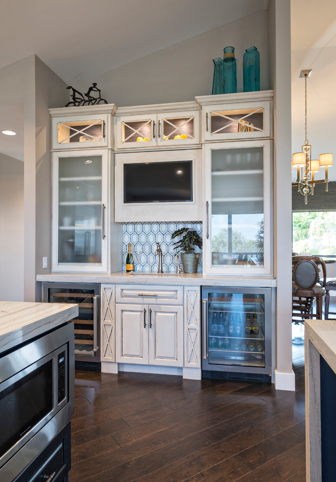 Photo of a mid-sized beach style u-shaped open plan kitchen in Miami with a farmhouse sink, raised-panel cabinets, beige cabinets, marble benchtops, stainless steel appliances and multiple islands.
