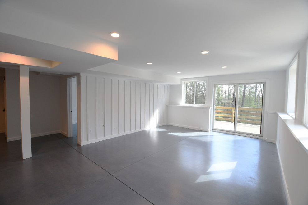 Large midcentury walk-out basement in New York with white walls, concrete floors, grey floor and panelled walls.