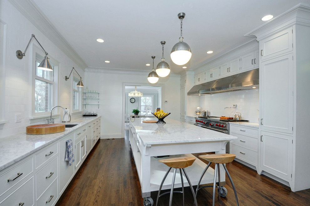 This is an example of a large transitional separate kitchen in Chicago with an undermount sink, recessed-panel cabinets, white cabinets, marble benchtops, white splashback, subway tile splashback, panelled appliances, medium hardwood floors, with island and brown floor.