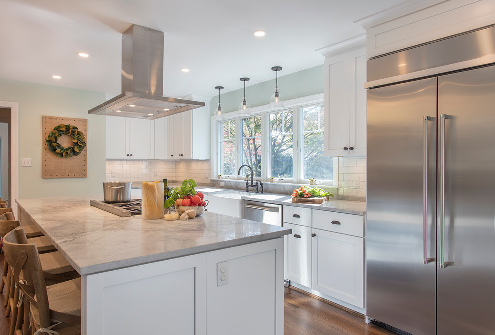 Large transitional l-shaped eat-in kitchen in DC Metro with a farmhouse sink, shaker cabinets, white cabinets, marble benchtops, white splashback, ceramic splashback, stainless steel appliances, medium hardwood floors and with island.