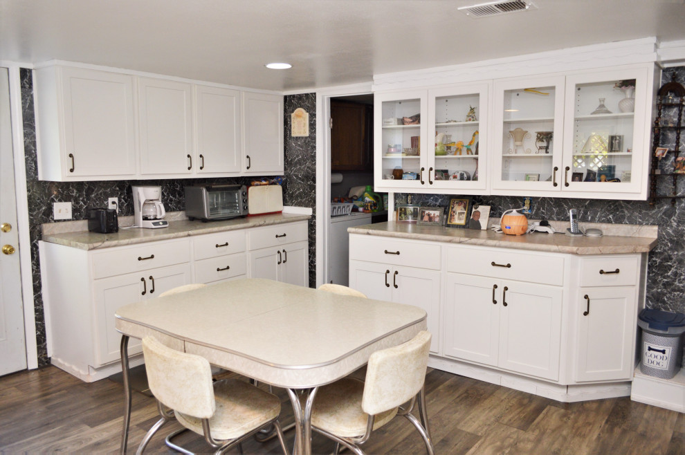 Large country u-shaped eat-in kitchen in Chicago with a drop-in sink, shaker cabinets, white cabinets, laminate benchtops, black splashback, white appliances, laminate floors, no island, brown floor and beige benchtop.