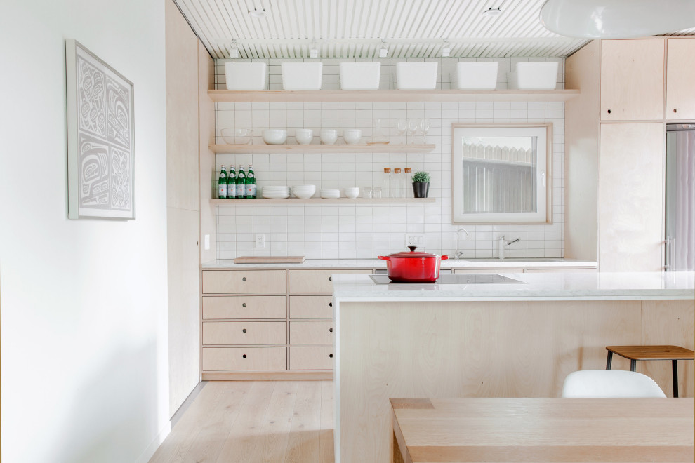 Inspiration for a small scandinavian galley open plan kitchen in Calgary with an undermount sink, flat-panel cabinets, light wood cabinets, quartz benchtops, white splashback, ceramic splashback, stainless steel appliances, light hardwood floors, with island, white benchtop and beige floor.
