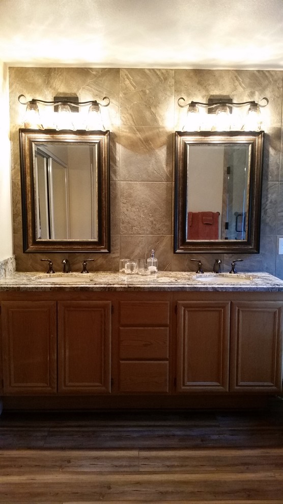 Inspiration for a mid-sized traditional master bathroom in Las Vegas with beaded inset cabinets, brown cabinets, a one-piece toilet, beige tile, porcelain tile, beige walls, vinyl floors, an undermount sink, granite benchtops, brown floor, brown benchtops, an alcove tub and a hinged shower door.