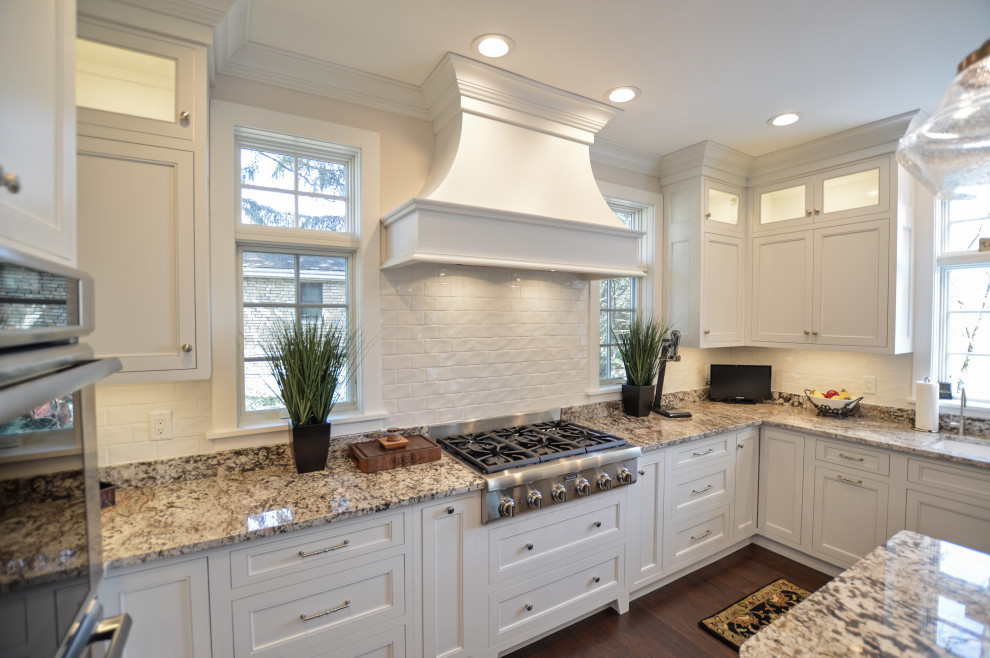 Example of a transitional dark wood floor and brown floor eat-in kitchen design with an undermount sink, shaker cabinets, white cabinets, granite countertops, white backsplash, ceramic backsplash, stainless steel appliances, an island and beige countertops