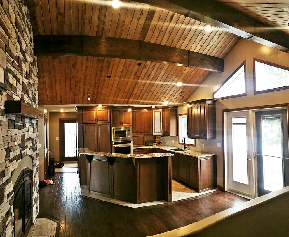 Mid-sized mountain style l-shaped dark wood floor and brown floor eat-in kitchen photo with an undermount sink, shaker cabinets, brown cabinets, granite countertops, stainless steel appliances and an island