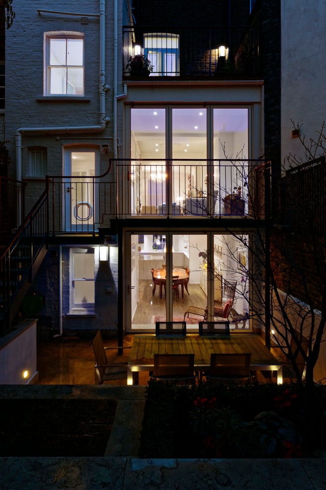 Photo of a mid-sized contemporary two-storey glass white townhouse exterior in London with a flat roof.