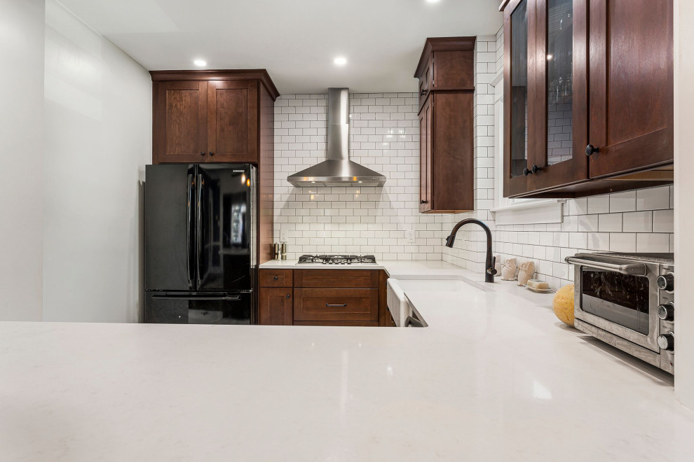 Inspiration for a large timeless porcelain tile and white floor kitchen remodel in Philadelphia with a farmhouse sink, shaker cabinets, brown cabinets, quartz countertops, white backsplash, subway tile backsplash, stainless steel appliances, a peninsula and white countertops