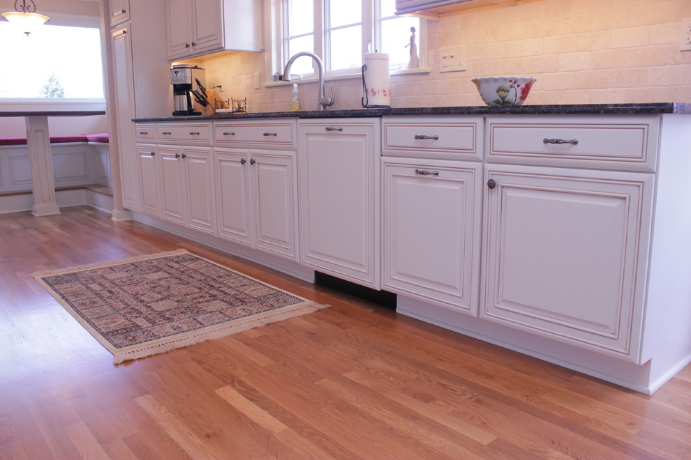 Inspiration for a large transitional galley medium tone wood floor and brown floor eat-in kitchen remodel with a double-bowl sink, recessed-panel cabinets, white cabinets, granite countertops, beige backsplash, travertine backsplash, stainless steel appliances and no island