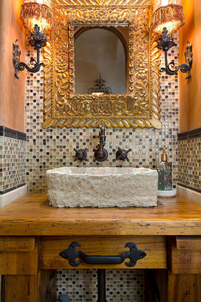 Design ideas for a small mediterranean powder room in San Diego with stone tile, a vessel sink, wood benchtops, furniture-like cabinets, medium wood cabinets, orange walls and brown benchtops.