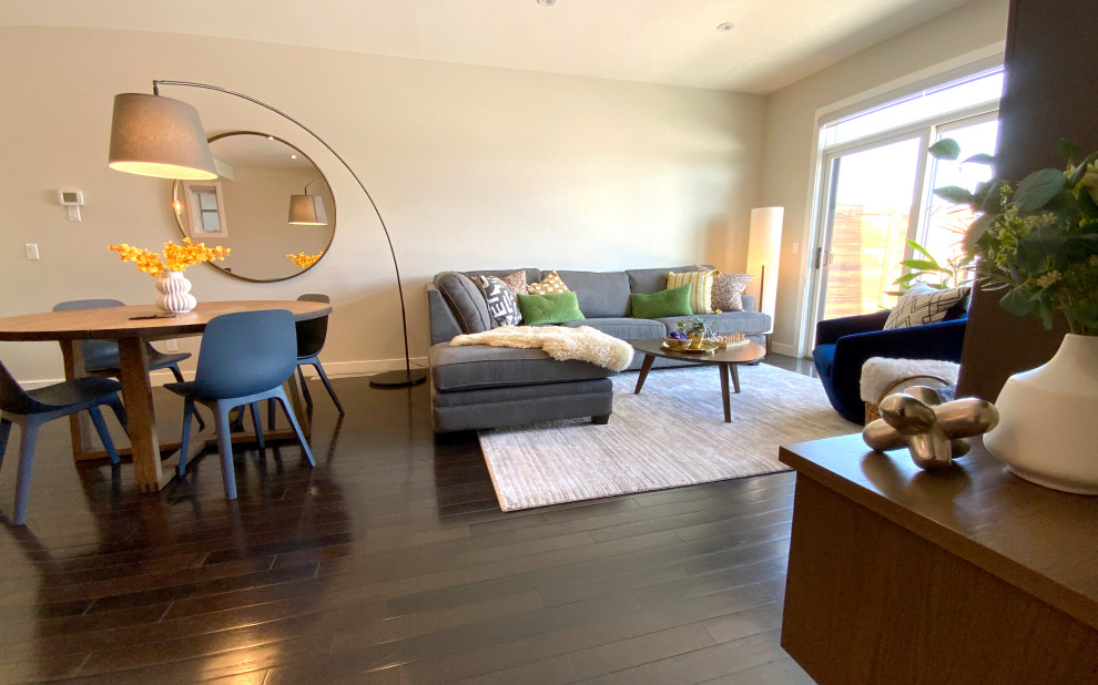 Kleines Modernes Wohnzimmer mit beiger Wandfarbe, dunklem Holzboden, Kamin, Kaminumrandung aus Stein, TV-Wand und braunem Boden in Calgary