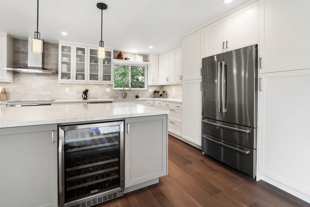Mid-sized transitional l-shaped kitchen pantry in Other with a double-bowl sink, shaker cabinets, white cabinets, quartz benchtops, beige splashback, subway tile splashback, stainless steel appliances, medium hardwood floors, with island, brown floor and beige benchtop.