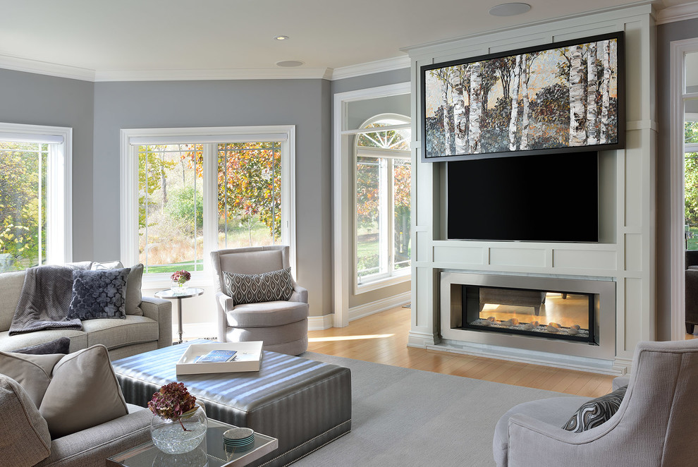 Inspiration for a large transitional family room in Toronto with grey walls, light hardwood floors, a two-sided fireplace, a wood fireplace surround and a wall-mounted tv.