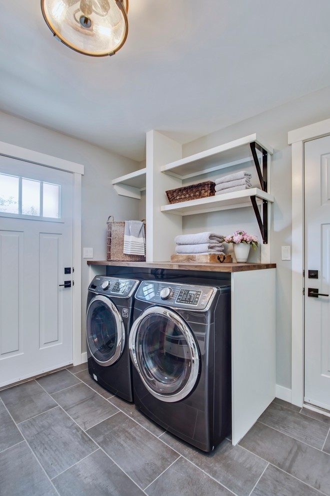 Design ideas for a mid-sized transitional utility room in Calgary with wood benchtops, grey walls, porcelain floors, a side-by-side washer and dryer and grey floor.