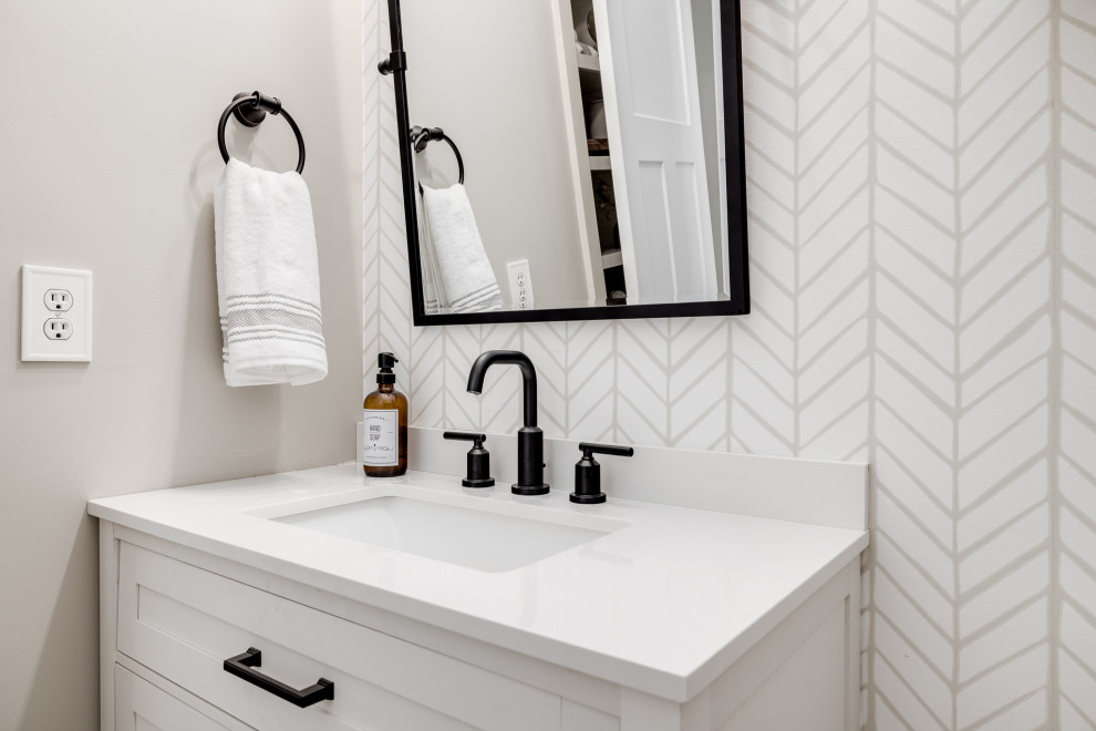 Example of a mid-sized transitional vinyl floor, beige floor and wallpaper powder room design in Other with shaker cabinets, white cabinets, a one-piece toilet, beige walls, an undermount sink, quartz countertops, white countertops and a freestanding vanity