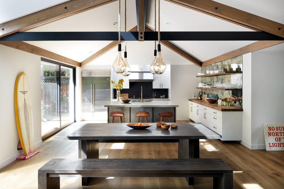 Photo of a beach style eat-in kitchen in San Francisco with flat-panel cabinets, white cabinets, black splashback, stainless steel appliances, medium hardwood floors, with island, grey benchtop, exposed beam and vaulted.