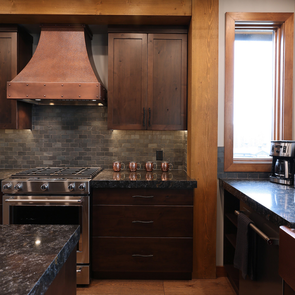 Photo of a country open plan kitchen in Vancouver with a farmhouse sink, shaker cabinets, medium wood cabinets, quartzite benchtops, black splashback, slate splashback, stainless steel appliances, medium hardwood floors, with island, brown floor, black benchtop and wood.