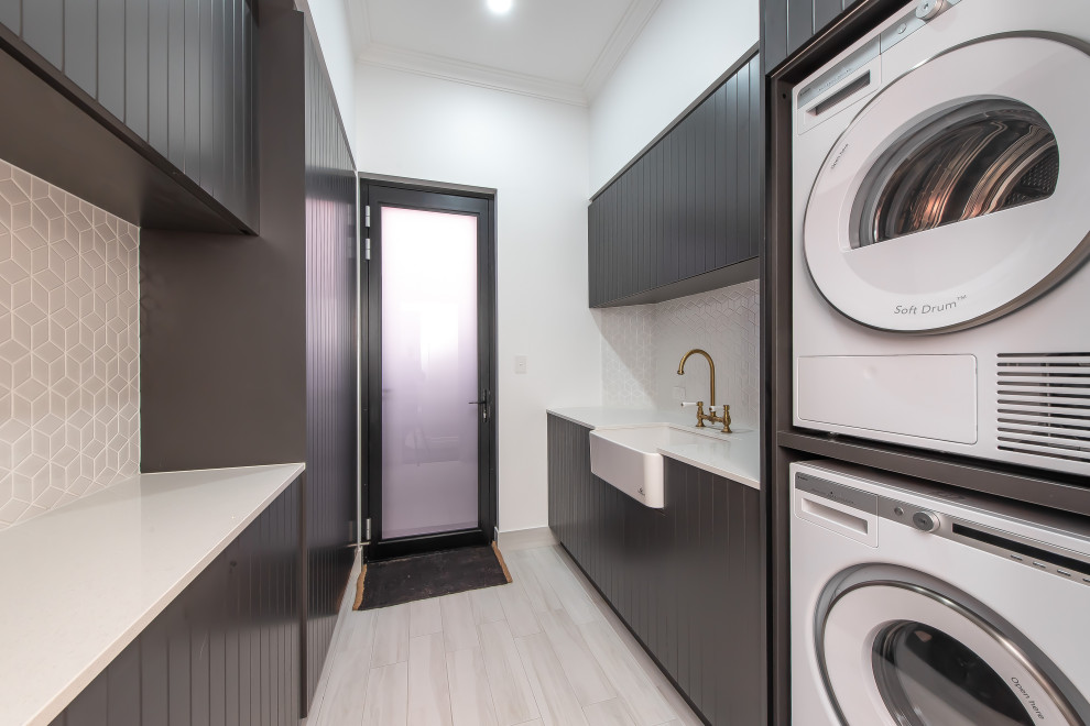 Design ideas for a contemporary galley separated utility room in Perth with a belfast sink, black cabinets, composite countertops, white splashback, mosaic tiled splashback, white walls, porcelain flooring, a stacked washer and dryer, grey floors and white worktops.