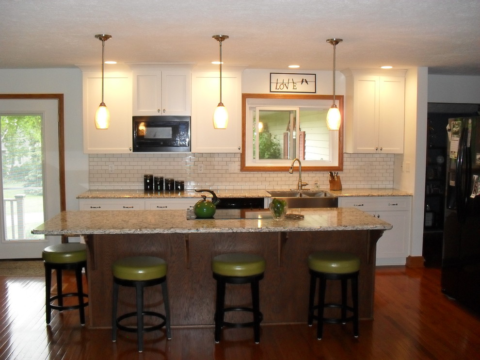 Inspiration for a large transitional medium tone wood floor open concept kitchen remodel with white cabinets, white backsplash, black appliances, an island, a farmhouse sink, recessed-panel cabinets and subway tile backsplash