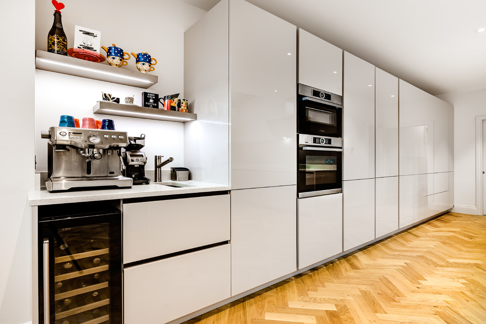 Large galley kitchen in London with a double-bowl sink, quartzite benchtops, glass sheet splashback, stainless steel appliances, light hardwood floors, a peninsula, yellow floor and white benchtop.