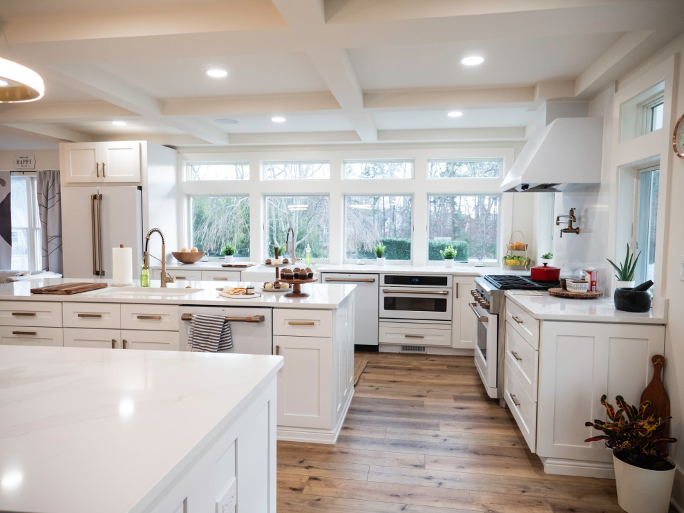 Huge minimalist laminate floor, brown floor and coffered ceiling open concept kitchen photo in Philadelphia with a farmhouse sink, shaker cabinets, white cabinets, wood countertops, white backsplash, quartz backsplash, white appliances, two islands and white countertops