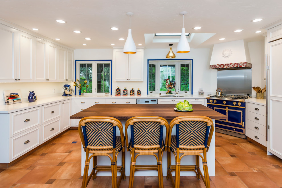 Photo of a large mediterranean u-shaped open plan kitchen in San Francisco with a double-bowl sink, white cabinets, with island, panelled appliances, terra-cotta floors, brown floor, recessed-panel cabinets, solid surface benchtops and white benchtop.