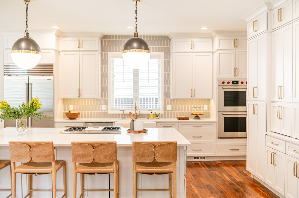 Open concept kitchen - large transitional l-shaped dark wood floor and brown floor open concept kitchen idea in Denver with a farmhouse sink, shaker cabinets, beige cabinets, quartz countertops, beige backsplash, ceramic backsplash, stainless steel appliances, an island and white countertops