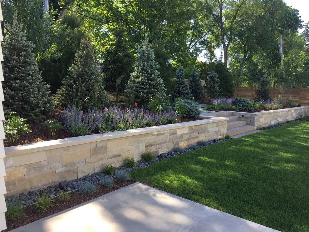 Modern backyard full sun xeriscape in Minneapolis with a retaining wall and natural stone pavers for summer.