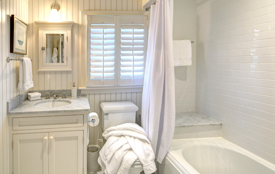 This is an example of a small traditional bathroom in Boston with an undermount sink, beaded inset cabinets, white cabinets, marble benchtops, an alcove tub, a shower/bathtub combo, a one-piece toilet, white tile, subway tile, white walls and marble floors.