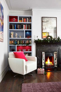 White chair with pink throw pillow next to fireplace 